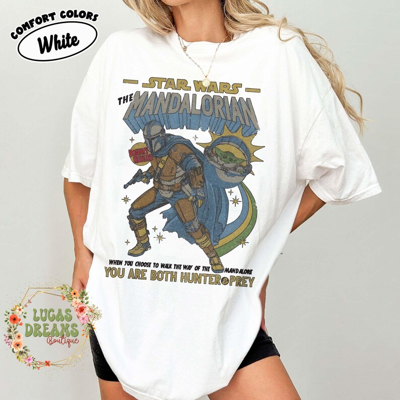 Puede incluir: Una camiseta blanca de manga corta con un estampado gr&aacute;fico de The Mandalorian y Grogu. El texto dice Star Wars The Mandalorian, Bounty Hunter y When you choose to walk the way of the Mandalore you are both hunter and prey.