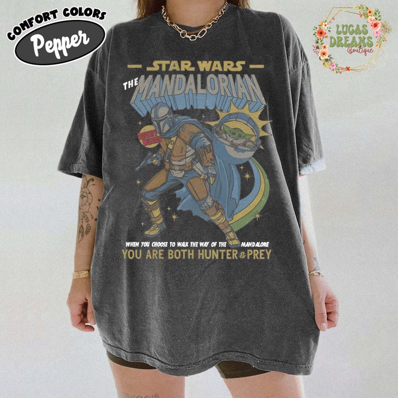 Puede incluir: Una camiseta de manga corta gris carb&oacute;n con un estampado gr&aacute;fico de The Mandalorian y Grogu. El dise&ntilde;o incluye el texto Star Wars The Mandalorian y la frase When you choose to walk the way of the Mandalore you are both hunter & prey.