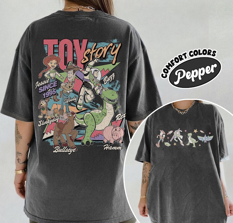 May include: Dark grey t-shirt with a vibrant Toy Story character graphic, including Woody, Buzz, and Rex. The back of the shirt features the words "Toy Story" and "Jessie Since 1995". The shirt also has the words "Comfort Colors Pepper" on the right side.