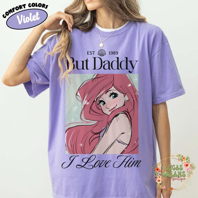 May include: Violet Comfort Colors t-shirt featuring a graphic of a cartoon character with pink hair. The shirt has the text "But Daddy I Love Him" and "Est 1989". A floral design is visible on the bottom right.