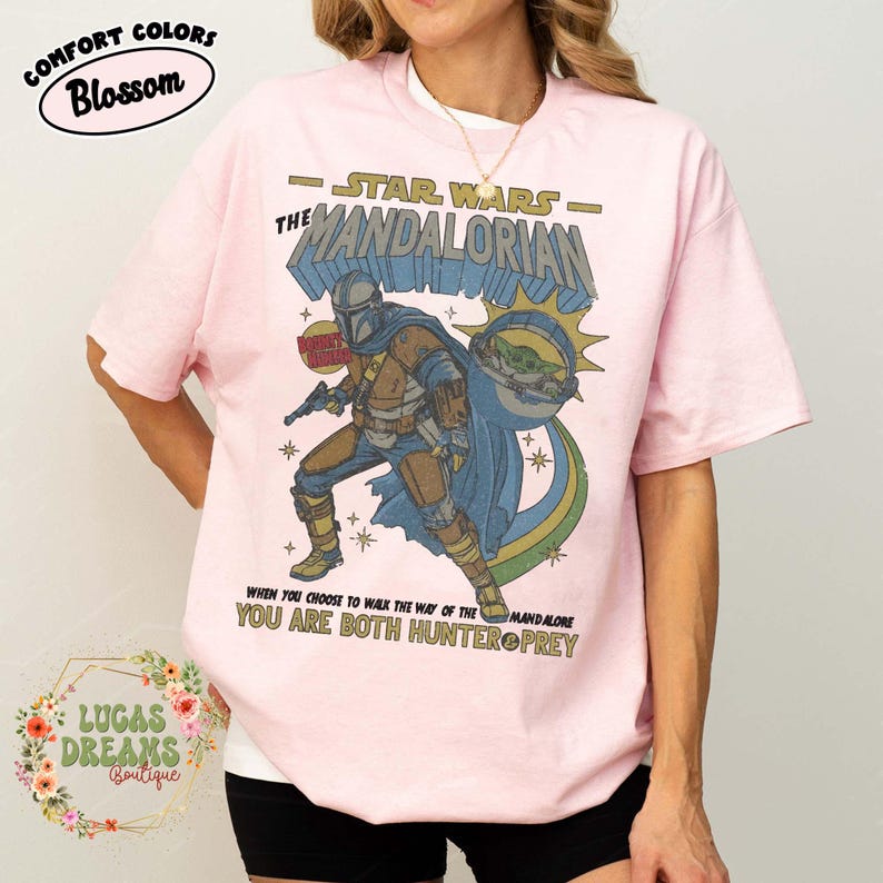 Puede incluir: Una camiseta rosa claro con un estampado gr&aacute;fico de The Mandalorian y Grogu. El dise&ntilde;o incluye el texto "STAR WARS THE MANDALORIAN" y "WHEN YOU CHOOSE TO WALK THE WAY OF THE MANDALORE YOU ARE BOTH HUNTER OR PREY" en un estilo vintage.