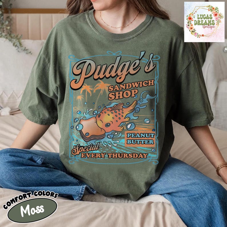 Pu&ograve; includere: T-shirt Comfort Colors verde muschio con grafica retr&ograve; per "Pudge's Sandwich Shop". Il design include un'illustrazione di sandwich al burro di arachidi, palme e il testo "Special Every Thursday."