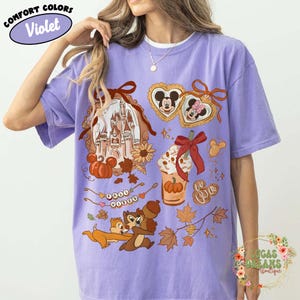 May include: Violet Comfort Colors t-shirt with a fall-themed graphic. The design includes a castle, pumpkins, Mickey and Minnie Mouse, Chip and Dale, and fall leaves. The shirt also has the words "Fall Vibes".