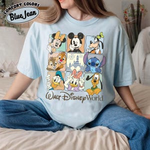 K&ouml;nnte beinhalten: Hellblaues T-Shirt mit einem Rastermuster, das Disney-Figuren wie Micky Maus, Minnie Maus und Donald Duck zeigt. Der Text "Walt Disney World" ist unten aufgedruckt. Das Shirt hat auch den Text "Comfort Colors Blue Jean" oben.