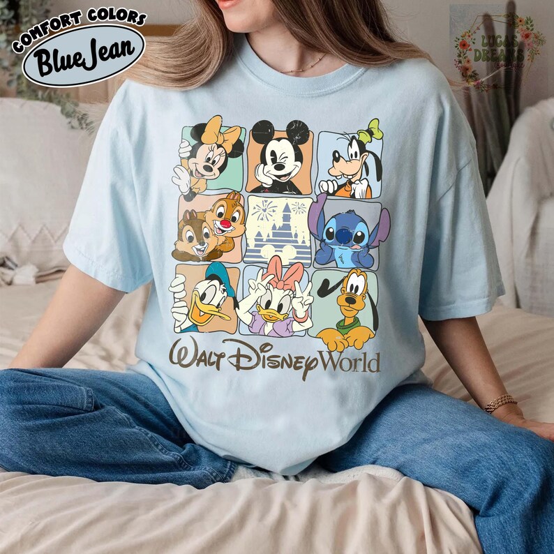 K&ouml;nnte beinhalten: Hellblaues T-Shirt mit einem Rastermuster, das Disney-Figuren wie Micky Maus, Minnie Maus und Donald Duck zeigt. Der Text "Walt Disney World" ist unten aufgedruckt. Das Shirt hat auch den Text "Comfort Colors Blue Jean" oben.