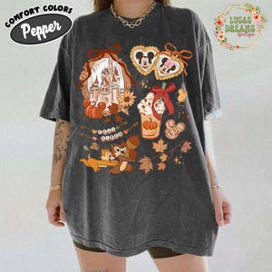 May include: Dark gray Comfort Colors t-shirt with a Disney-themed graphic. The design includes a castle, pumpkins, Mickey and Minnie Mouse cookies, a pumpkin spice latte, Chip and Dale, and autumn leaves. The shirt has the text "Pepper" on it.