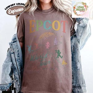 Puede incluir: Camiseta color espresso con la palabra "EPCOT" en letras coloridas. La camiseta presenta un gr&aacute;fico de la esfera EPCOT y personajes de dibujos animados. Las palabras "World Tour" est&aacute;n impresas debajo. La camiseta es parte de la colecci&oacute;n Comfort Colors.