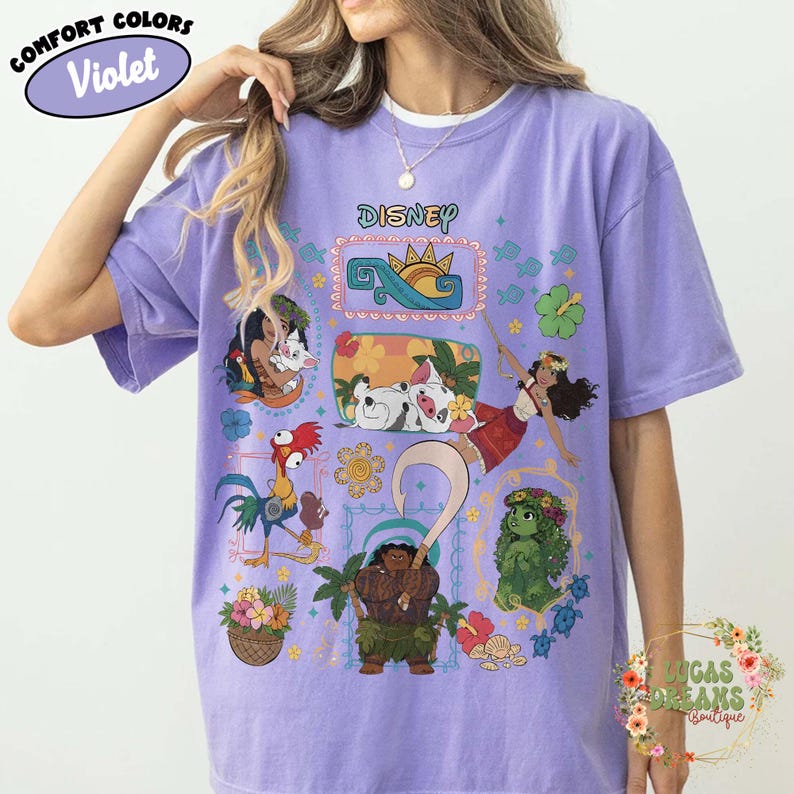May include: A lilac Comfort Colors t-shirt with Disney characters. The design includes Moana, Maui, and Pua, with the Disney logo. The shirt has a crew neck and short sleeves. The graphic is set against a light purple background. The shirt is a comfortable fit.