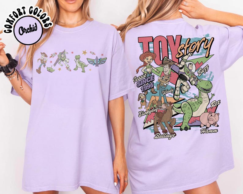 May include: A lilac t-shirt with characters from the animated film "Toy Story." The front of the shirt shows a line of characters, while the back has a larger graphic with the film's title and more characters. The text "Since 1995" is also visible.