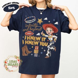 May include: A navy blue t-shirt featuring a graphic print of a cowgirl character, brown cowboy boots, a red hat, and alphabet blocks. The text reads "infinity and beyond", "YOU'VE GOT A FRIEND IN ME", and "I KNEW IT I KNEW YOU" in yellow and white.