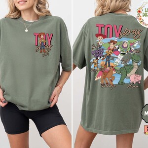 Peut inclure: T-shirt vert mousse avec le texte "Toy Story" et un dessin de Woody sur le devant. Le dos du t-shirt pr&eacute;sente divers personnages de Toy Story. Le t-shirt a une coupe ample et confortable.