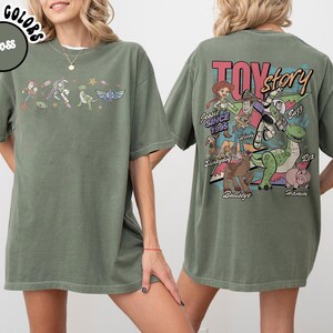 May include: Moss green t-shirt featuring Toy Story characters. The front displays a line of characters, while the back showcases a Toy Story graphic with characters and the text "Toy Story Since 1995". The shirt is made of a soft, comfortable material.