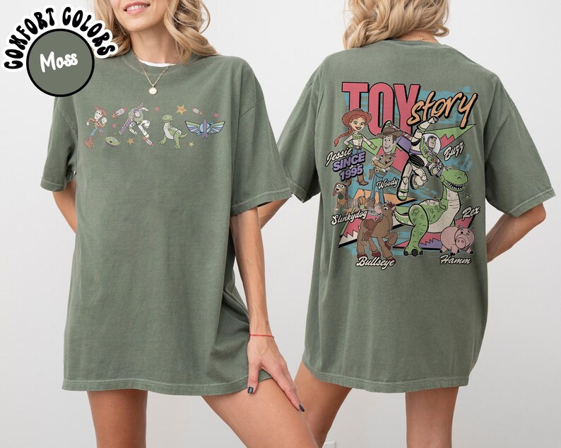 May include: Moss green t-shirt featuring Toy Story characters. The front displays a line of characters, while the back showcases a Toy Story graphic with characters and the text "Toy Story Since 1995". The shirt is made of a soft, comfortable material.