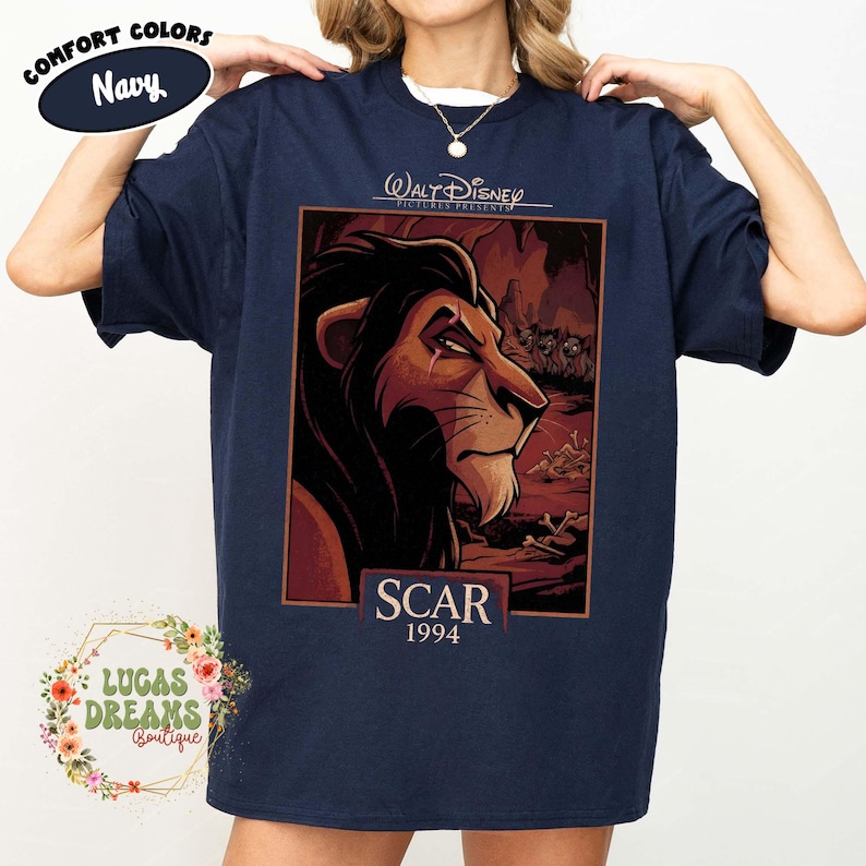 May include: A navy blue short-sleeve t-shirt featuring a graphic print of the character Scar from The Lion King. The design includes the text Walt Disney Pictures Presents, Scar, and 1994, set against a dark, rocky background with hyenas.