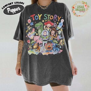 Pu&ograve; includere: T-shirt oversize grigio scuro con una grafica colorata dei personaggi del film "Toy Story". Il design include Woody, Buzz Lightyear, Rex e altri personaggi amati. La maglietta presenta la scritta "Toy Story".