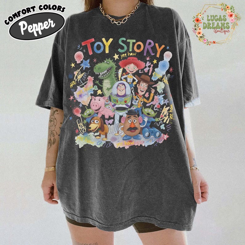 Pu&ograve; includere: T-shirt oversize grigio scuro con una grafica colorata dei personaggi del film "Toy Story". Il design include Woody, Buzz Lightyear, Rex e altri personaggi amati. La maglietta presenta la scritta "Toy Story".