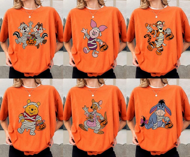 May include: Orange Halloween-themed t-shirts featuring various cartoon characters, including Chip and Dale, Piglet, Tigger, Winnie the Pooh, Roo, and Eeyore. Each character is dressed in a mummy costume and holding a jack-o'-lantern.