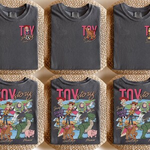Peut inclure: T-shirts gris fonc&eacute; avec l'inscription rose "TOY STORY" et divers motifs de personnages. Certains t-shirts pr&eacute;sentent de petits graphismes, tandis que d'autres affichent un motif plus grand avec des personnages comme Woody, Buzz et Rex.