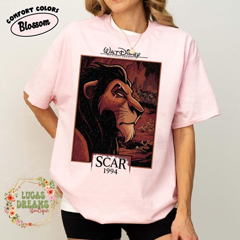 May include: A light pink t-shirt featuring a graphic print of the character Scar from The Lion King. The design includes the text Walt Disney Pictures Presents, Scar, and 1994. The illustration shows the lion in a dark, rocky landscape.