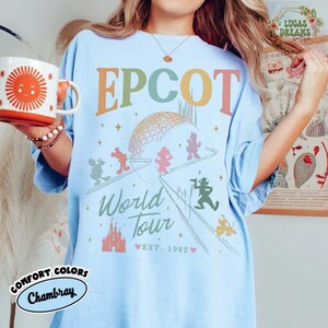 Puede incluir: Camiseta azul claro con estampado gr&aacute;fico de EPCOT World Tour. La camiseta presenta el logotipo de EPCOT en colores pastel, con Mickey Mouse y sus amigos. Las palabras "World Tour" y "Est. 1982" tambi&eacute;n est&aacute;n impresas en la camiseta.
