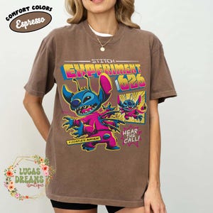 May include: Brown t-shirt featuring a graphic of Stitch from Lilo & Stitch, labeled "Experiment 626." The design includes Stitch in a pink jumpsuit with the text "A Complete Mayhem" and "Hear the Call!" The shirt is labeled "Comfort Colors Espresso."