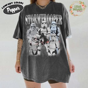 Puede incluir: Una camiseta de manga corta gris carb&oacute;n con un estampado gr&aacute;fico de cinco personajes Stormtrooper blancos de Star Wars. La palabra STORMTROOPER est&aacute; impresa en letras may&uacute;sculas blancas grandes sobre los personajes. Tiene cuello redondo.