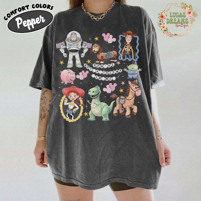 May include: Dark gray oversized t-shirt featuring colorful cartoon characters from the Toy Story movie. The shirt includes Buzz Lightyear, Woody, Jessie, and other characters. The text "You've Got a Friend in Me" is also visible.