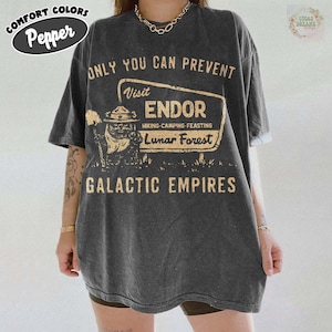 Puede incluir: Camiseta gris oscuro con el texto "ONLY YOU CAN PREVENT" encima de un letrero que dice "Visit ENDOR Hiking-Camping-Feasting Lunar Forest Galactic Empires". La camiseta tiene un aspecto vintage y las palabras "COMFORT COLORS Pepper" están en la parte superior izquierda.