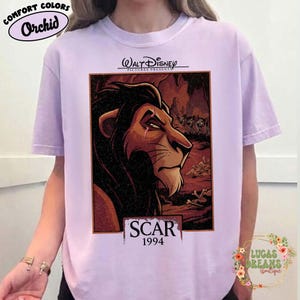 May include: A light purple t-shirt featuring a graphic print of the character Scar from The Lion King. The design includes the text Walt Disney Pictures Presents, Scar, and 1994. The character is depicted in profile against a dark, rocky background.