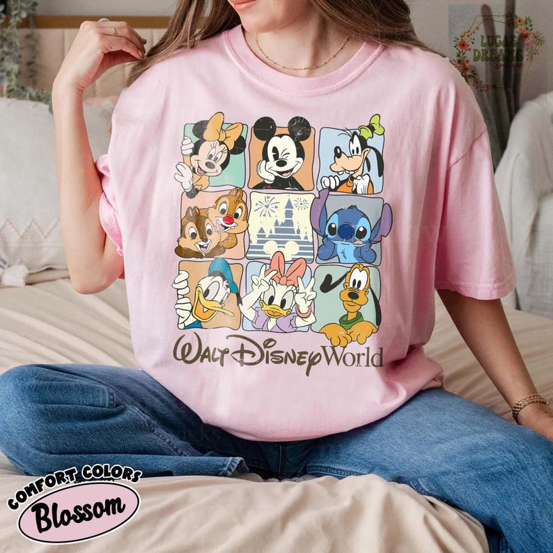 K&ouml;nnte beinhalten: Hellrosa T-Shirt mit einem Rastermuster von Disney-Figuren wie Mickey Mouse, Minnie Mouse und Donald Duck. Der Schriftzug "Walt Disney World" ist darunter aufgedruckt. Hergestellt aus Comfort Colors Blossom Stoff.