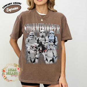 Puede incluir: Una camiseta de manga corta color marr&oacute;n espresso con un estampado gr&aacute;fico de cinco Stormtroopers blancos en varias poses. La palabra STORMTROOPER est&aacute; impresa en una fuente grande de estilo met&aacute;lico sobre los personajes.