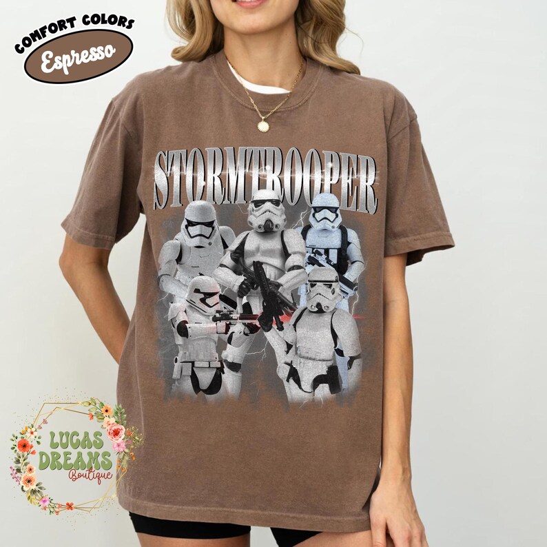 Puede incluir: Una camiseta de manga corta color marr&oacute;n espresso con un estampado gr&aacute;fico de cinco Stormtroopers blancos en varias poses. La palabra STORMTROOPER est&aacute; impresa en una fuente grande de estilo met&aacute;lico sobre los personajes.