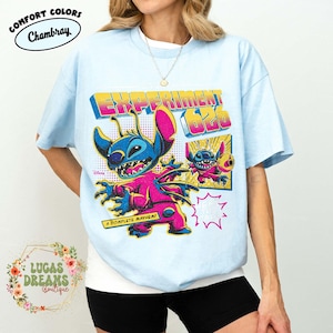 May include: Light blue t-shirt featuring a colorful graphic of the character Stitch from Disney's Lilo & Stitch. The design includes the text "EXPERIMENT 626" and "A COMPLETE MAYHEM!" in a retro style. The shirt is from the Comfort Colors brand.
