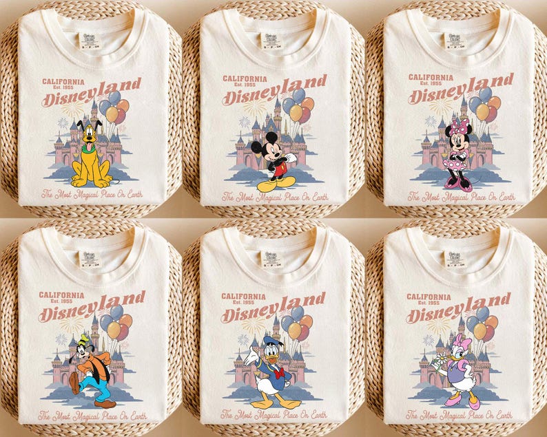 May include: Cream-colored t-shirts featuring Disneyland graphics with various Disney characters. Each shirt displays the Disneyland logo, a castle illustration, and the phrase "The Most Magical Place On Earth."