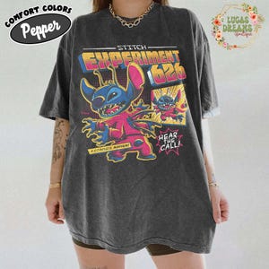 May include: Dark gray t-shirt featuring a colorful graphic of Stitch from Experiment 626. The design includes the text "STITCH EXPERIMENT 626", "A COMPLETE MAYHEM", and "HEAR THE CALL!". The shirt has a relaxed fit and the Comfort Colors Pepper logo.