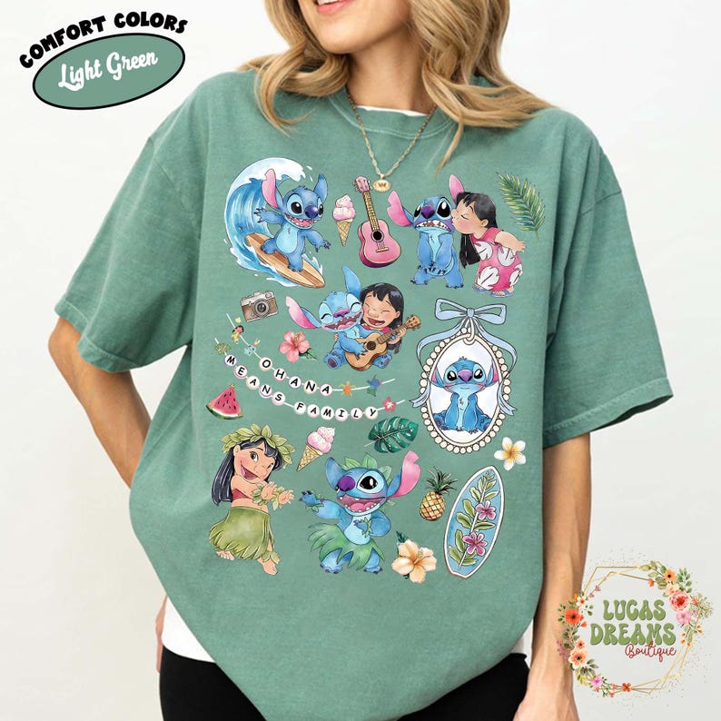 May include: Light green t-shirt featuring a collage of cartoon characters, including a blue alien. The design includes the text "OHANA MEANS FAMILY" and various tropical elements like flowers, surfboards, and ice cream cones. The shirt is labeled "Comfort Colors" and "Light Green".