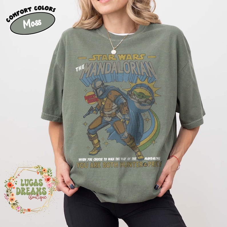 Puede incluir: Una camiseta de manga corta color verde musgo con un gr&aacute;fico de The Mandalorian y Grogu. El estampado incluye el texto STAR WARS THE MANDALORIAN y WHEN YOU CHOOSE TO WALK THE WAY OF THE MANDALORIAN YOU ARE BOTH HUNTER & PREY.