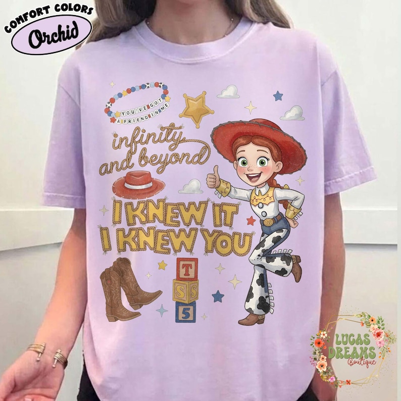 May include: A light purple t-shirt featuring a graphic of a cowgirl character with a red hat, brown boots, and a cow-print pattern. The design includes text reading infinity and beyond, I KNEW IT, I KNEW YOU, and YOU'VE GOT A FRIEND IN ME.