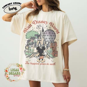 May include: Ivory-colored t-shirt with a graphic of the Walt Disney World castle, Spaceship Earth, and Mickey Mouse. The text "Walt Disney World" and "The happiest place on earth" are printed on the shirt. The shirt is from Lucas Dreams Boutique.