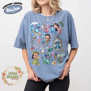 May include: Blue Comfort Colors t-shirt featuring a colorful graphic of Stitch and Lilo from the Disney movie Lilo & Stitch. The design includes the text "Ohana means family" and various tropical elements. The shirt also has the text "Blue Jean" and "Lucas Dreams Boutique".
