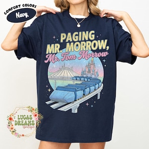 May include: Navy blue t-shirt featuring the text "Paging Mr. Morrow, Mr. Tom Morrow" and a graphic of a monorail, Space Mountain, and a castle. The shirt also has the words "Comfort Colors" and "Lucas Dreams Boutique".