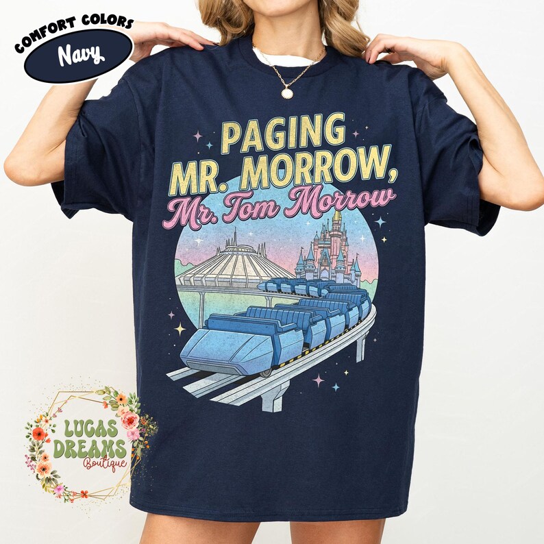 May include: Navy blue t-shirt featuring the text "Paging Mr. Morrow, Mr. Tom Morrow" and a graphic of a monorail, Space Mountain, and a castle. The shirt also has the words "Comfort Colors" and "Lucas Dreams Boutique".