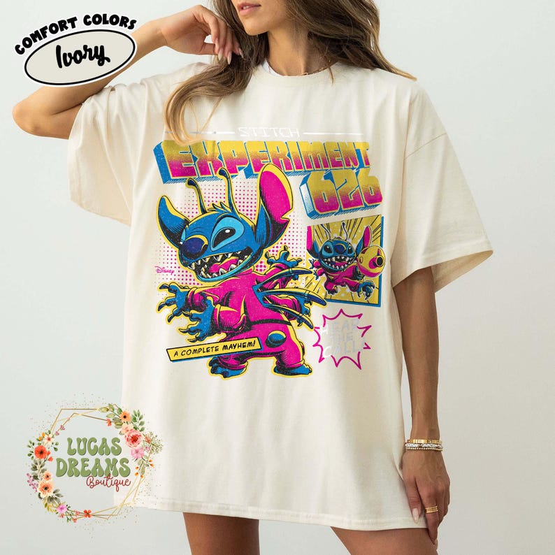 May include: Ivory-colored t-shirt featuring a graphic of Stitch from Disney's Lilo & Stitch. The design includes the text "EXPERIMENT 626" and "A COMPLETE MAYHEM!" in vibrant colors. The shirt has short sleeves and a relaxed fit.