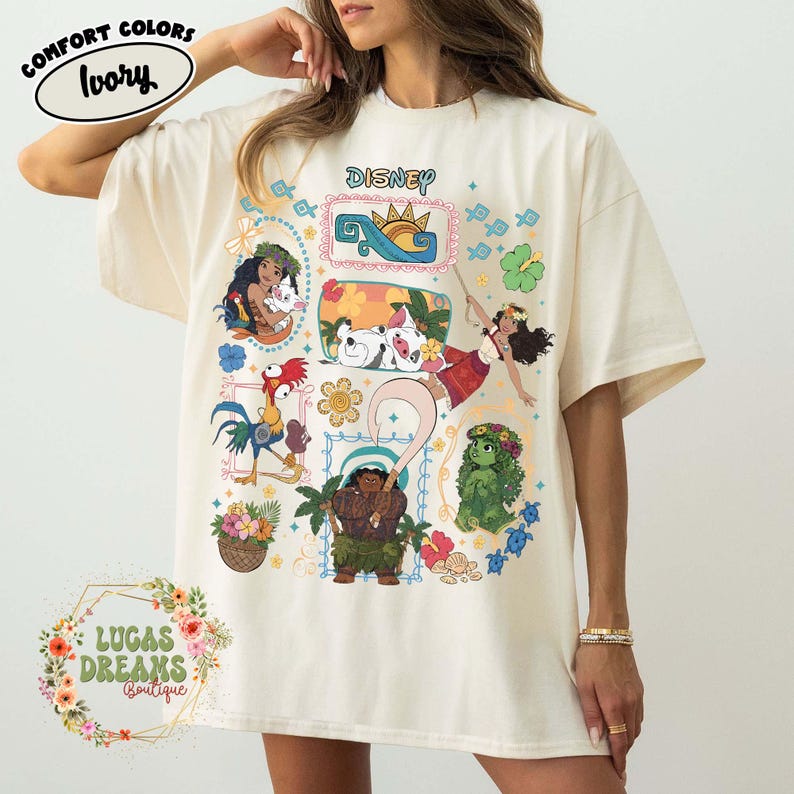 May include: Ivory-coloured t-shirt featuring Disney characters from the movie Moana. The shirt has a colourful graphic design with the word "Disney" at the top. The shirt is from Lucas Dreams Boutique.