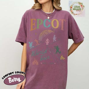 Puede incluir: Camiseta de color bayas con la palabra "EPCOT" en letras coloridas sobre un gr&aacute;fico de la geosfera Spaceship Earth y personajes de Disney. La camiseta tambi&eacute;n presenta las palabras "World Tour" y un gr&aacute;fico de castillo.