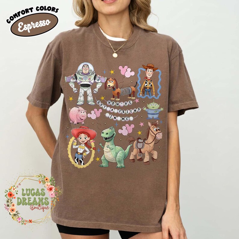 May include: Brown t-shirt featuring various Toy Story characters, including Buzz Lightyear, Woody, and Rex. The phrase "You've Got a Friend in Me" is printed on the shirt. The shirt also has the text "Comfort Colors Espresso" and "Lucas Dreams Boutique".