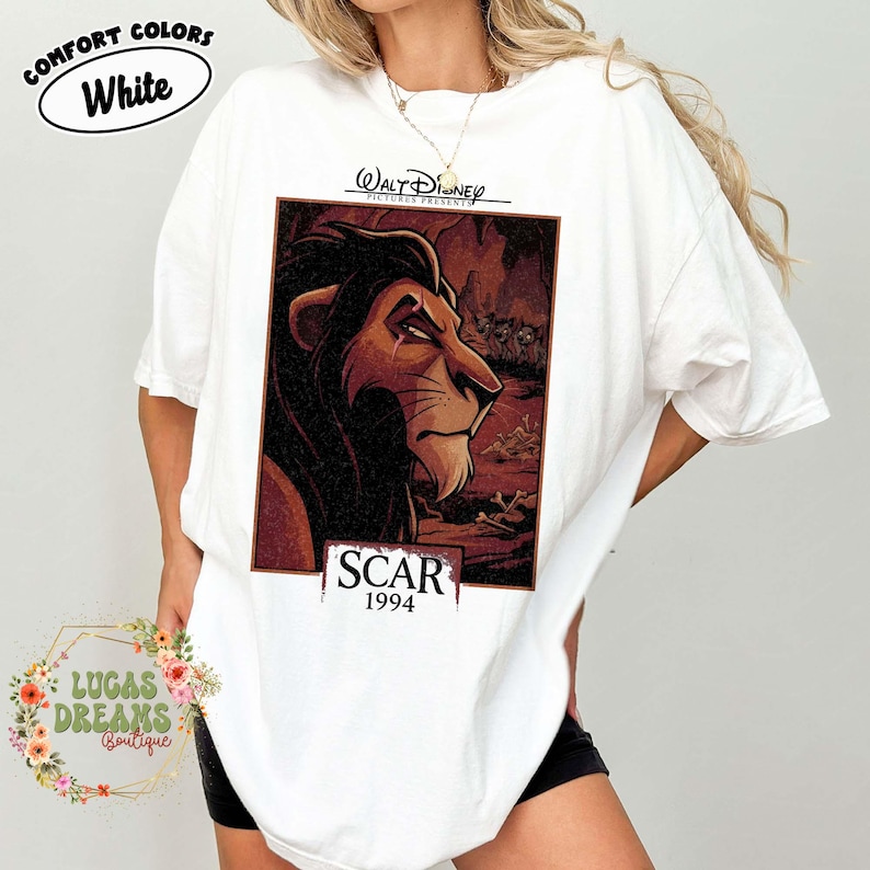 May include: A white short-sleeved t-shirt featuring a rectangular graphic print of the character Scar from The Lion King. The print includes the text Walt Disney Pictures Presents, Scar, and 1994. The shirt has a crew neckline and loose fit.