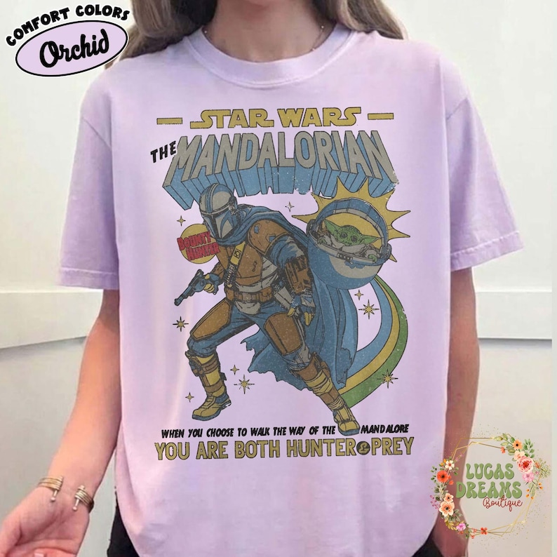 Puede incluir: Una camiseta de color morado claro con un estampado gr&aacute;fico de The Mandalorian y Grogu. El texto dice Star Wars The Mandalorian, Bounty Hunter y When you choose to walk the way of the Mandalore you are both hunter and prey.