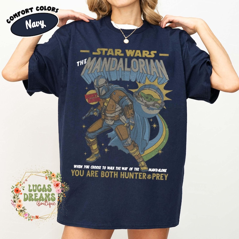 Puede incluir: Una camiseta azul marino de manga corta con un estampado gr&aacute;fico de The Mandalorian y Grogu. El texto dice Star Wars The Mandalorian, Bounty Hunter y When you choose to walk the way of the Mandalore you are both hunter and prey.