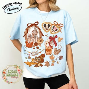 May include: Light blue Comfort Colors Chambray t-shirt with a fall-themed graphic. The design includes a castle, pumpkins, Mickey and Minnie Mouse, Chip and Dale, and fall leaves. The text "Lucas Dreams Boutique" is also visible.
